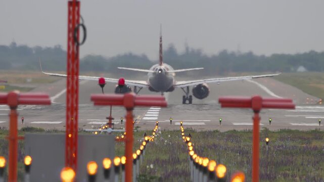 Commercial passenger airplane rolling on international airport runway after landing, with runway lights glowing in foreground, telephoto shot.