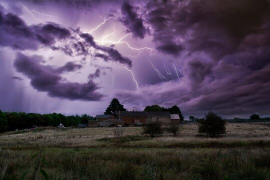 Dramatic Purple Lightning Storm Over Rural Farmhouse and Rolling Fields at Night