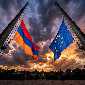 national flag of armenia and flag of european union wave against cloudy sunset sky above evening city symbolizing european integration and international state partnership