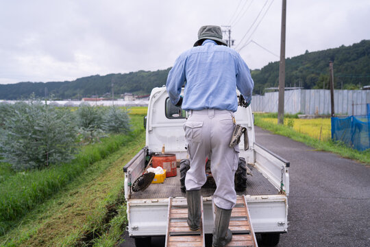 Farmer loading a mower onto a kei truck using an aluminum ramp on a rural road