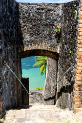 View of the tropical turquoise sea and a palm tree through a historic stone archway and staircase...