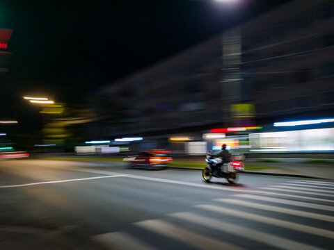 Motorcyclist riding through city street at night with motion blur. Speed and movement in night city traffic. Transportation and urban lifestyle concept.
