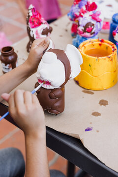 hand of artist kid girl with brush painting ceramic figure at terrace in latin America