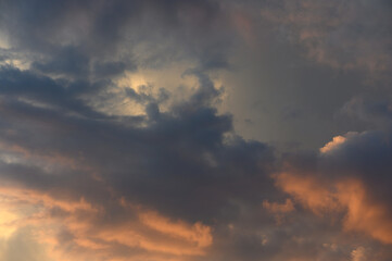 Fototapeta premium An atmospheric landscape photograph of a dramatic evening sky filled with heavy, dark storm clouds illuminated by warm golden and orange sunset rays breaking through.