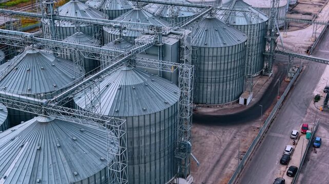 Modern industrial agricultural facility featuring numerous cylindrical metal grain silos. Metal grain elevator complex with the road and red truck moving by.
