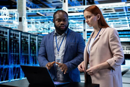 Engineering team coordinates data center backups on a laptop, reviewing recovery protocols and upgrading equipment components together in a server farm.