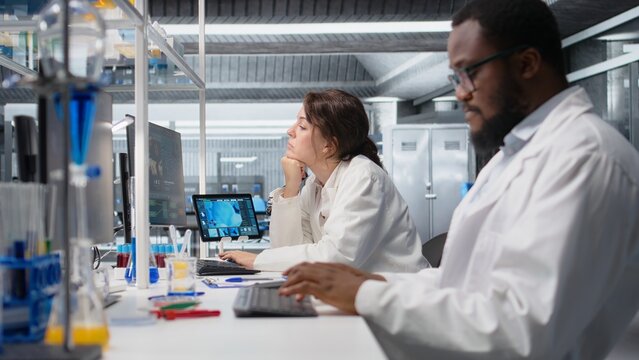 Diagnostic lab manager oversees scientists reviewing molecular models on a PC, supervising researchers using bioengineering software on a computer in a medical laboratory during analysis.