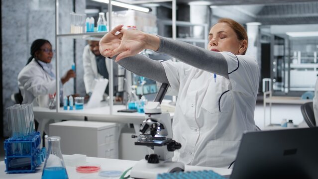 Histology technician correcting posture while using microscope