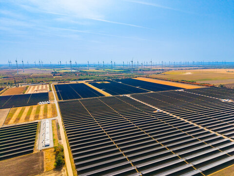 High angle view of massive solar panel rows in countryside. Geometric patterns of photovoltaic modules stretch across dry terrain under blue sky.