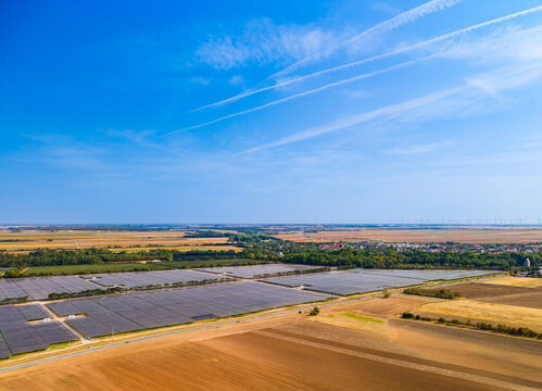 Solar farm array, photovoltaic panels in rural landscape background. Aerial view of large solar panel power plant on agricultural fields under blue sky with sunlight