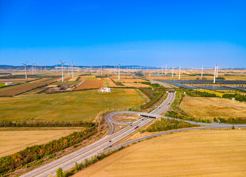 Highway interchange near wind turbines and solar farm. High angle view of road intersection with wind turbines and solar panels in field.