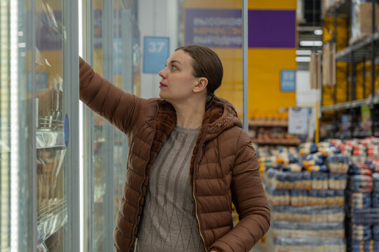 Woman examines product date carefully. Customer verifies item shelf life thoroughly. Woman diligently reviews product expiration information before selecting item for purchase in supermarket