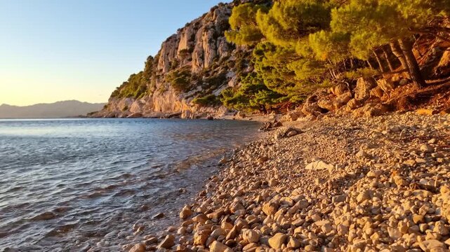 The water of the Adriatic Sea breaking on beautiful wild pebble beach with pine trees and rocky cliffs on Makarska riviera, Croatia