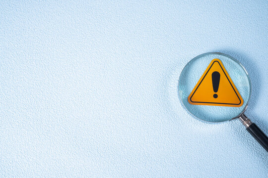 A magnifying glass shows a yellow warning sign with a black exclamation mark