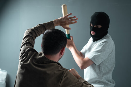 A masked bandit beats a man with a bat.