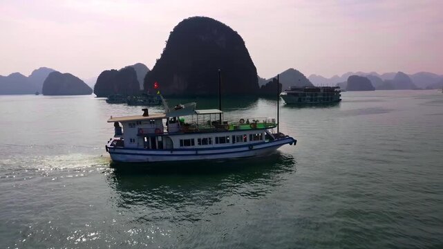 4K Aerial Drone View of Cruise Boat Sailing Past Limestone Karst Islands in Ha Long Bay, Vietnam