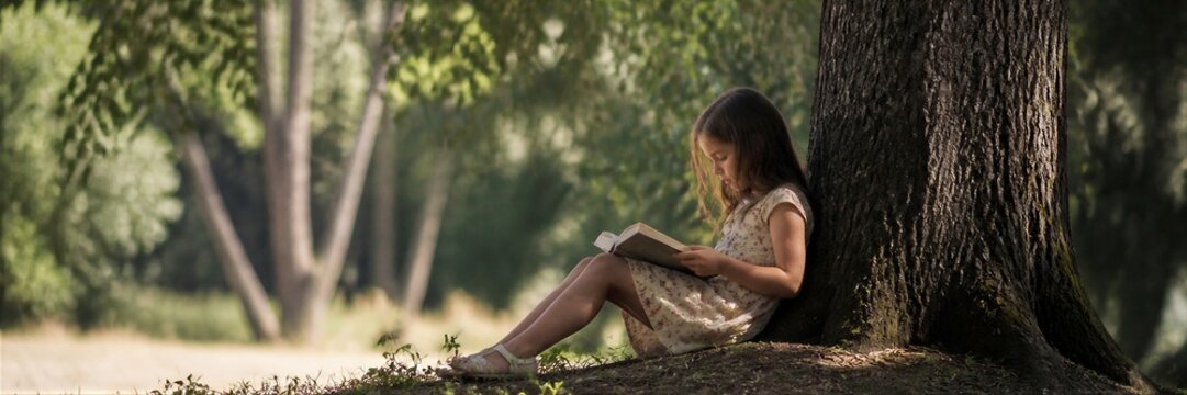 Girl reading book under big tree in summer park. Child enjoying literature outdoors in nature. Childhood education, imagination and love of reading concept.