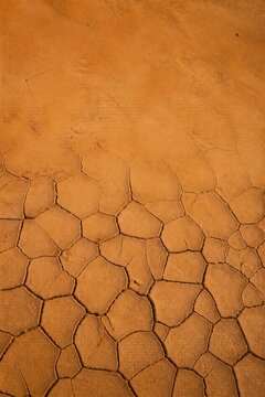 Cracked dry earth texture with ochre orange soil background. Drought and climate change concept.