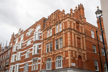 Fototapeta premium Historic Red Brick Building With Ornate Architecture Under Cloudy Sky