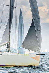 Fototapeta premium sailing regatta in the Gulf of Finland at sunny day, Yachtsmen are sitting amicably on board of the sailing boat, magic splashing water, teamwork, reflections