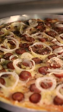 POV of a pizza maker checking a pizza inside an electric oven. Close-up of a pepperoni, mozzarella, and onion pizza. The pizzaiolo rotates the pizza inside the hot oven. Preparing a homemade pizza. 