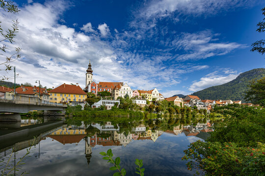 Historic town skyline of Frohnleiten with the parish church tower and colorful buildings reflected in the Mur River in Styria, Austria
