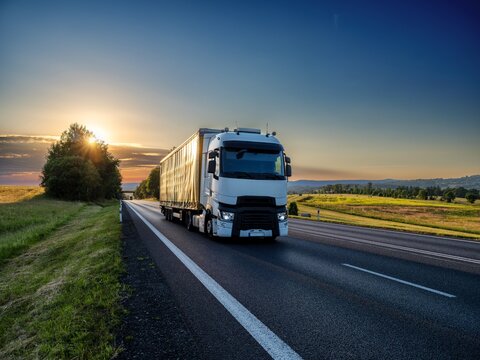 White truck driving on asphalt road in rural landscape at sunset