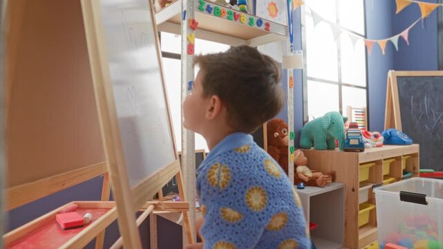 Boy writing on whiteboard with marker in a colorful playroom building, holding eraser at easel and surrounded by toys and shelves; curiosity learning.