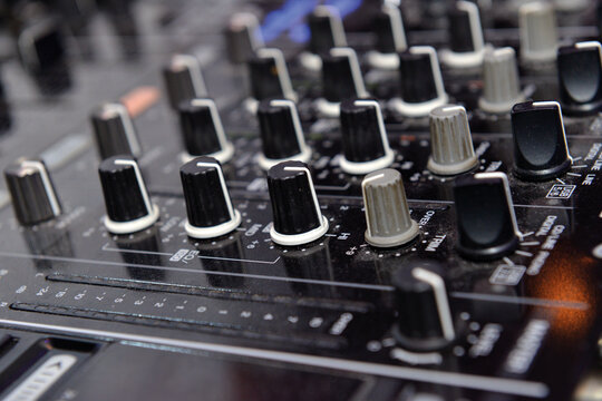 Angled macro shot of multiple black knobs on an audio mixer desk creating a repetitive industrial pattern.
