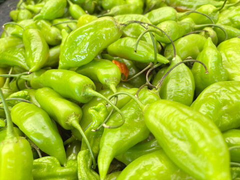 A glossy pile of bright green pepperoncini peppers with curled stems, fresh and tangy at the market