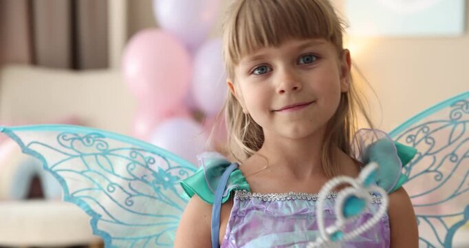 Cute little girl in beautiful costume with wings waving magic wand at home. Camera moving forward and backwards