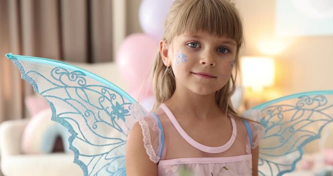 Cute little girl in fairy costume with wings waving magic wand at home. Camera moving forward and backwards