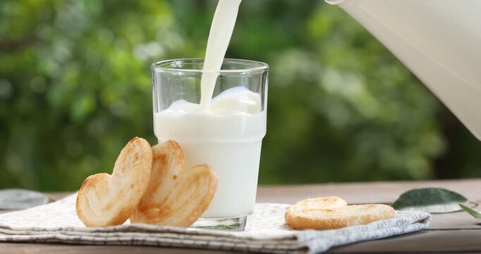 Woman pouring fresh milk into glass at wooden table, closeup
