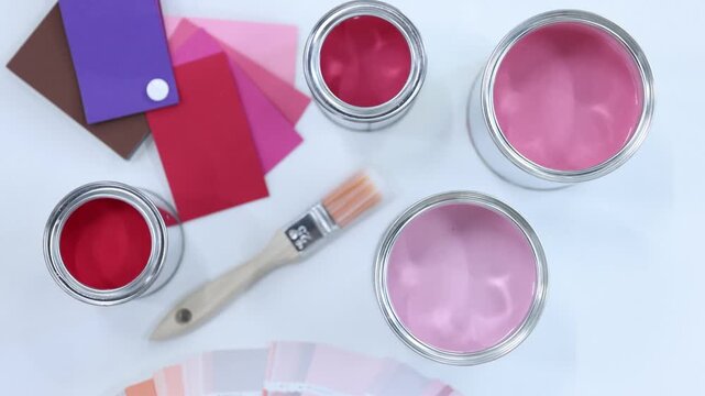 Cans with paint in shades of pink, brush and color palettes on white background, flat lay. Camera moving in