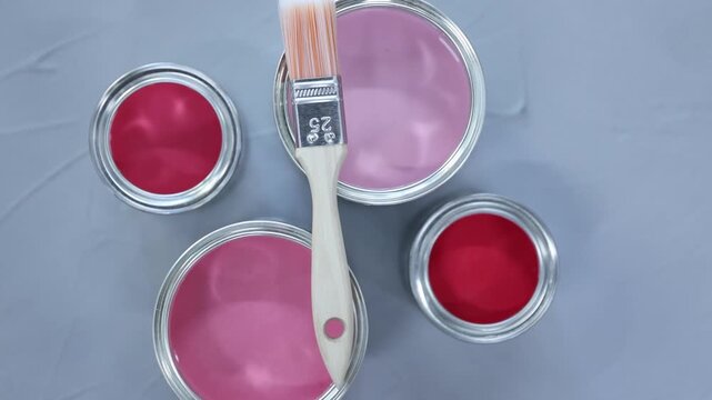 Cans with paint in shades of pink and brush on grey background, flat lay