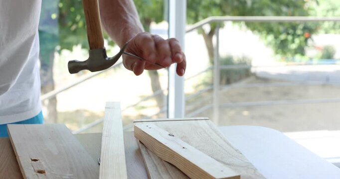 Man pulling metal nail out of wooden plank at table indoors, closeup