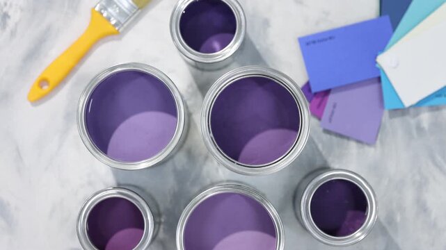 Cans with paint in shades of purple, brush and color palettes on textured table, flat lay. Camera moving in