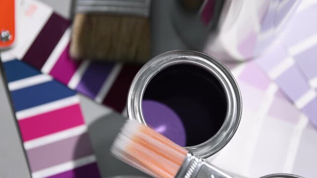 Cans with paint in shades of purple, brush and color palettes on light grey table, above view. Camera moving in