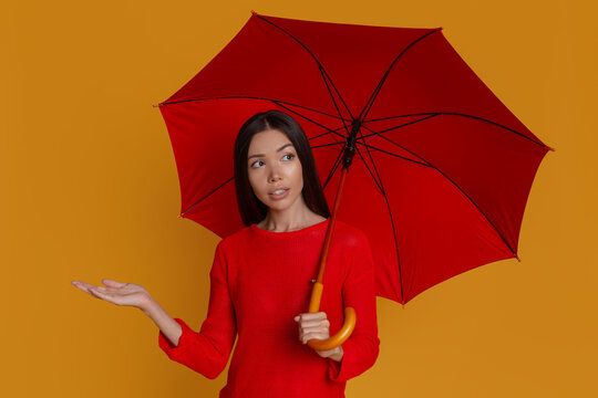 Confused woman checking for rain under umbrella with copy space