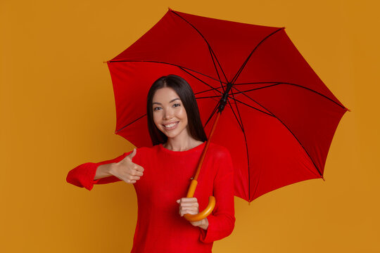 Smiling woman with umbrella giving thumbs up for protection