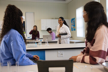 Indian instructor teaching teenage students in lab coat holding tablet in school lab with flasks © WavebreakMediaMicro
