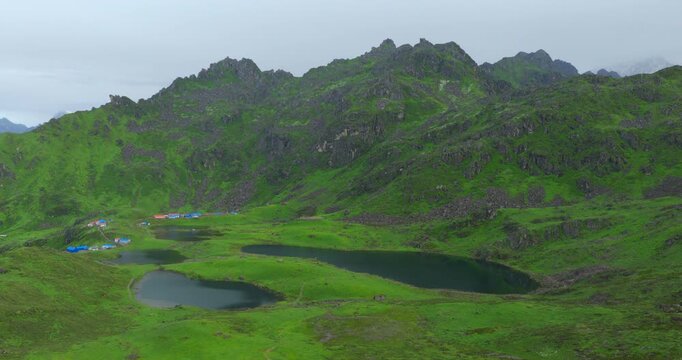 Aerial shot across the sacred five lakes of Panchpokhari, Sindhupalchowk, Nepal of the vivid green alpine slopes, dark rocky crags, and subtle cloud cover