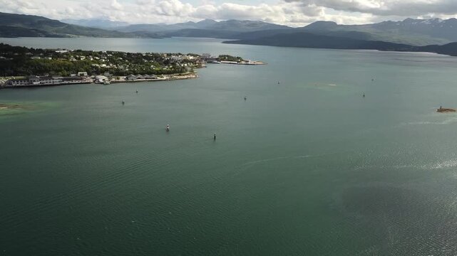 Aerial drone footage pans left across the open fjord and distant mountains near Senja, Norway, revealing the Gisund Bridge leading toward the coastal town of Finnsnes