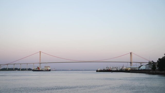 A scenic view of the iconic Maputo-Katembe Bridge spanning the waters near the Port with cargo ships and harbor activity creating a striking industrial waterfrone scene