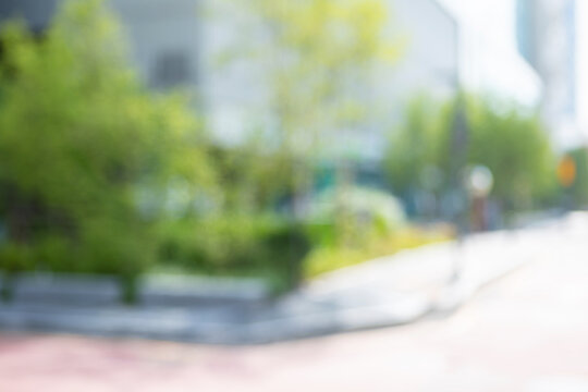 Abstract blurred modern downtown public plaza background with a building frontage and green trees garden