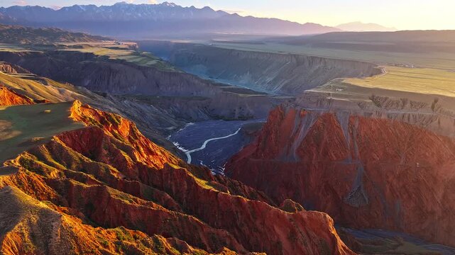 Aerial view of a winding braided river flowing through a deep rocky gorge at sunset in Anjihai Grand Canyon, Xinjiang, China