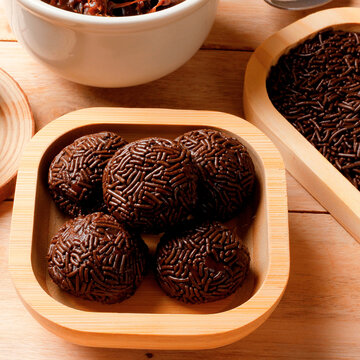 Chocolate brigadeiro with chocolate sprinkle topping, a traditional Brazilian sweet served on a bamboo tray on a light wood surface.