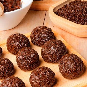 Homemade chocolate brigadeiro coated in sprinkles, presented in a rustic style on a bamboo tray atop a wooden table.