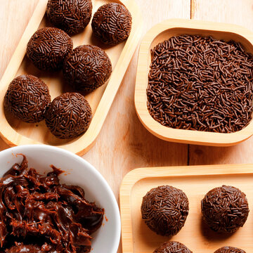 Classic Brazilian chocolate brigadeiro finished with sprinkles, served on a bamboo tray as part of a culinary arrangement on a wooden table.