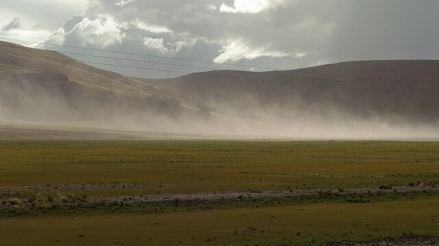 Sand storm moving by wind on grass field like wall with mountains background, 4k slow motion footage environment concept b roll shot.